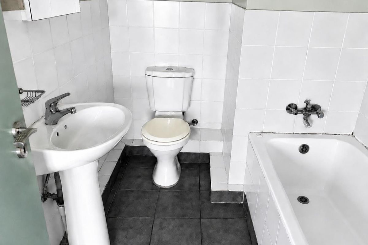 A functional bathroom featuring a pedestal basin, standard toilet, and a bathtub with white wall tiling and dark floor tiles.