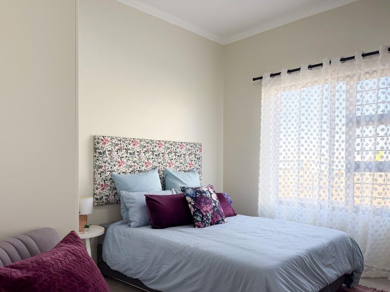 A well-lit bedroom featuring a window with decorative curtains and neutral wall finishes.