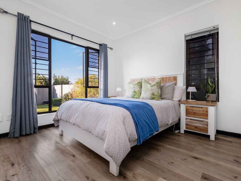 A bright and well-maintained bedroom featuring modern laminate flooring, large windows providing natural light, and recessed ceiling lighting.