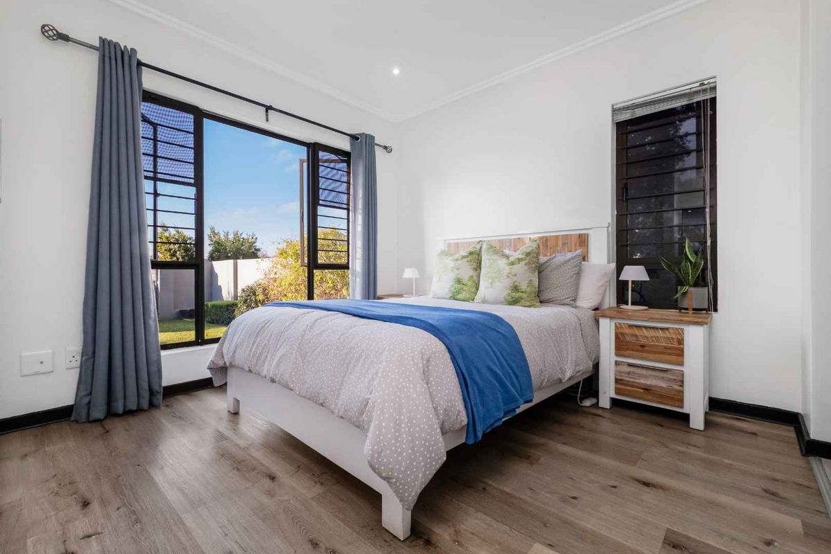 A bright and well-maintained bedroom featuring modern laminate flooring, large windows providing natural light, and recessed ceiling lighting.