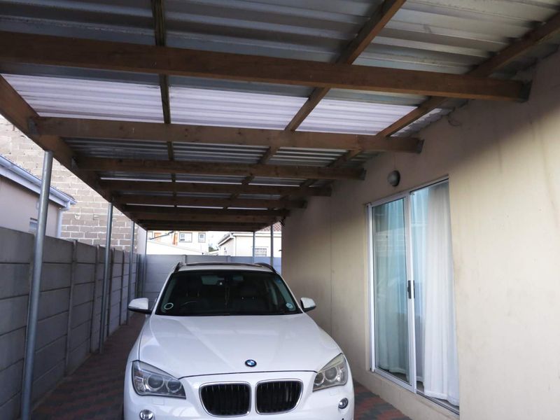 A covered carport area featuring a corrugated roof with timber rafters, adjacent to a sliding glass door entrance.