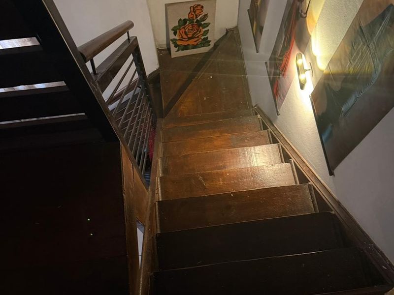 A view looking down a wooden staircase featuring a metal handrail and wall-mounted lighting.