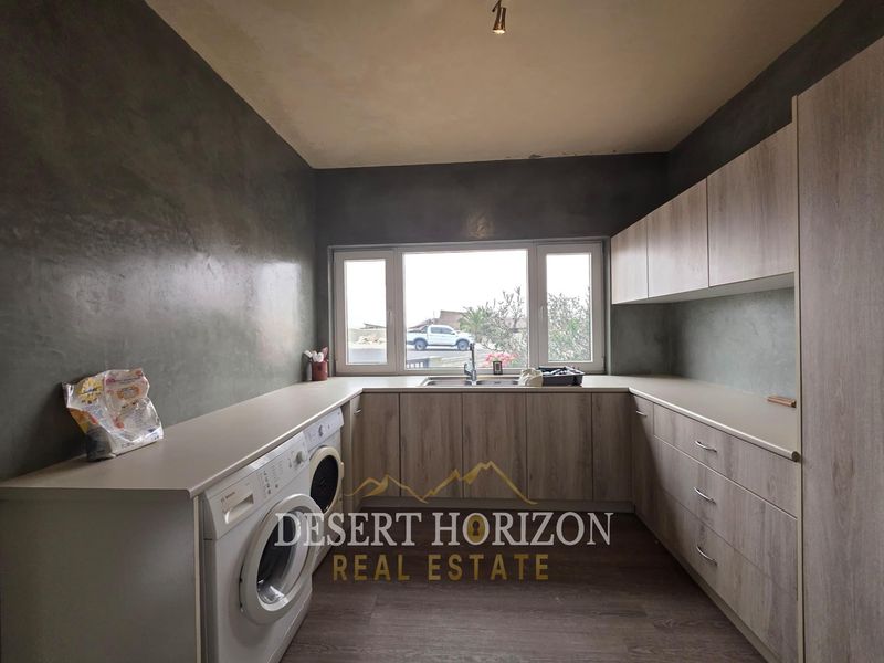 A functional laundry room featuring ample built-in cabinetry, laminate countertops, a stainless steel sink, and space for laundry appliances.