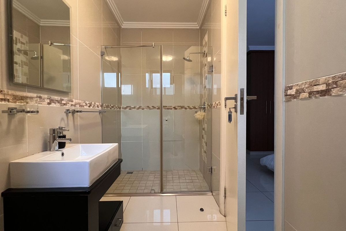 Modern bathroom featuring a glass-enclosed shower, contemporary vanity with basin, and neutral wall tiling with decorative mosaic accents.