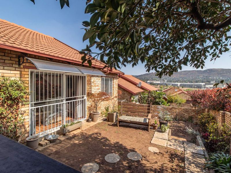 Rear exterior view of a townhouse featuring a brick facade, tiled roof, security gate, and a private garden area with scenic mountain views.