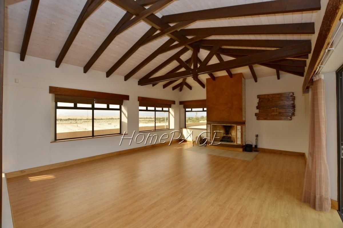 Spacious living room featuring high vaulted ceilings with exposed timber beams, a large central fireplace, and expansive windows offering natural light and scenic views.