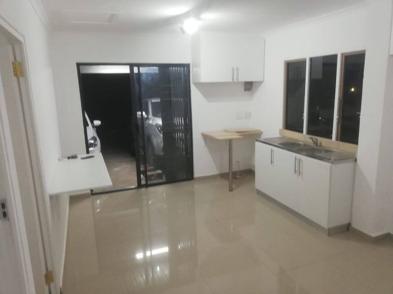 A compact, empty kitchen area featuring white cabinetry, a stainless steel sink, tiled flooring, and direct access to an outdoor space via a sliding door.