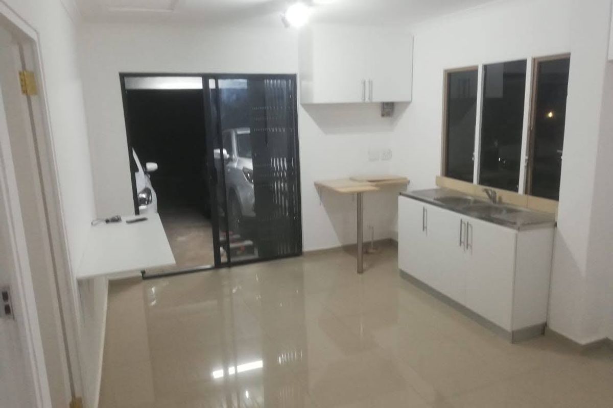 A compact, empty kitchen area featuring white cabinetry, a stainless steel sink, tiled flooring, and direct access to an outdoor space via a sliding door.