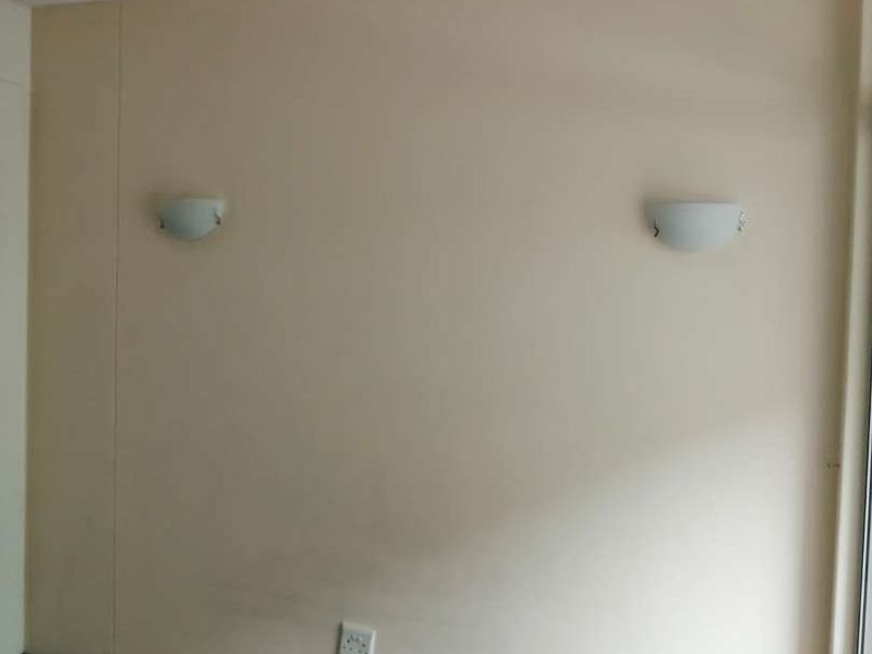 An empty bedroom featuring wall-mounted light fixtures, neutral wall finishes, and carpeted flooring, ready for personalization.