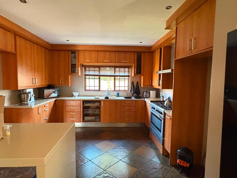 A functional kitchen featuring extensive wooden cabinetry, built-in oven with gas hob, tiled flooring, and a window providing natural light.