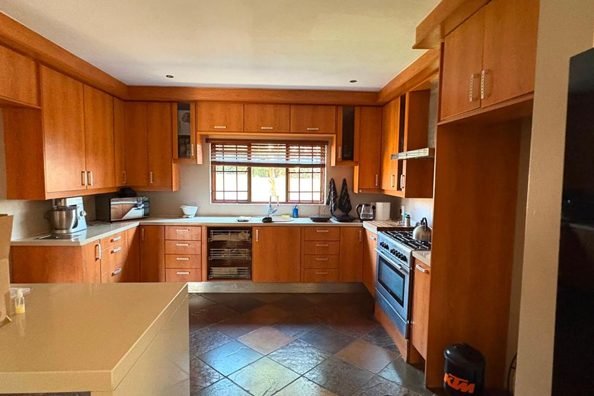 A functional kitchen featuring extensive wooden cabinetry, built-in oven with gas hob, tiled flooring, and a window providing natural light.