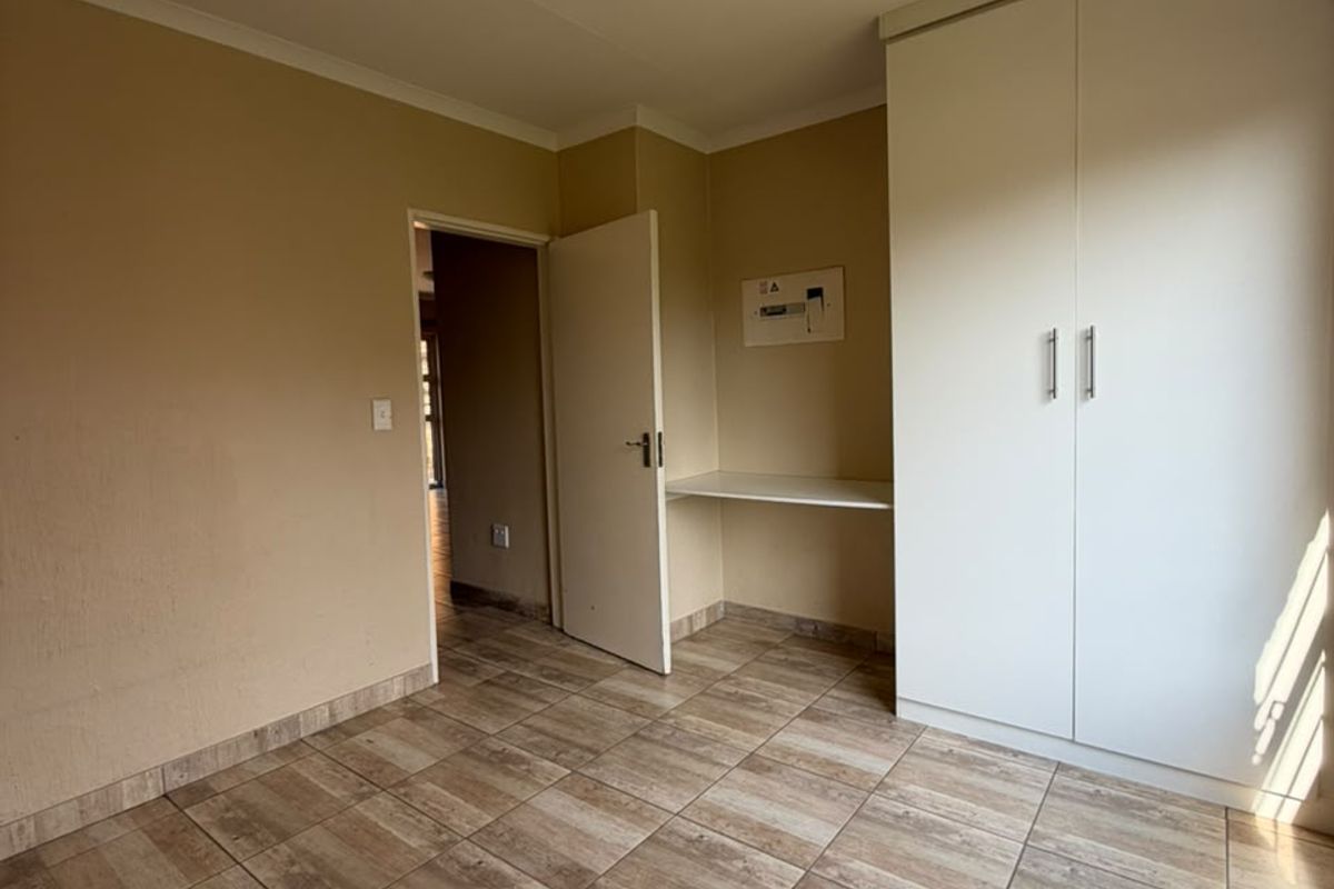 A vacant bedroom featuring tiled flooring, a built-in wardrobe, and a small integrated desk area.