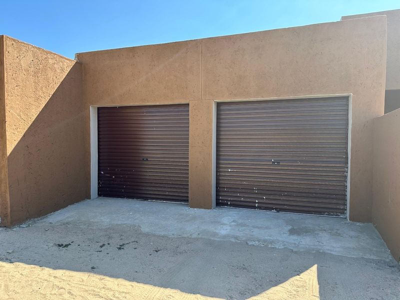 A double garage featuring brown roller doors and a concrete driveway, set against a textured stucco exterior wall.