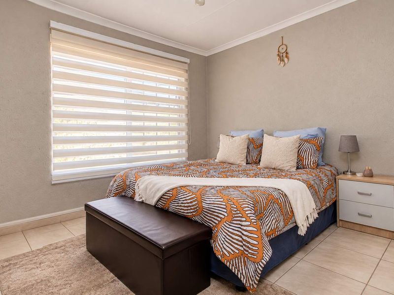 A well-maintained bedroom featuring neutral wall tones, tiled flooring, and modern roller blinds, providing a clean and comfortable living space.