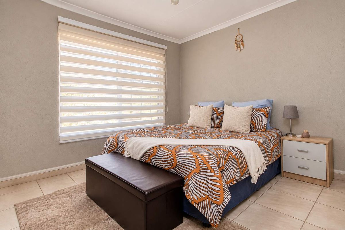 A well-maintained bedroom featuring neutral wall tones, tiled flooring, and modern roller blinds, providing a clean and comfortable living space.