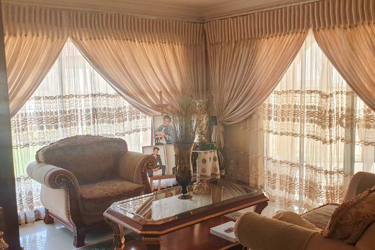 A living room featuring tiled flooring, recessed ceiling lighting, and large sliding glass doors with floor-to-ceiling curtains.