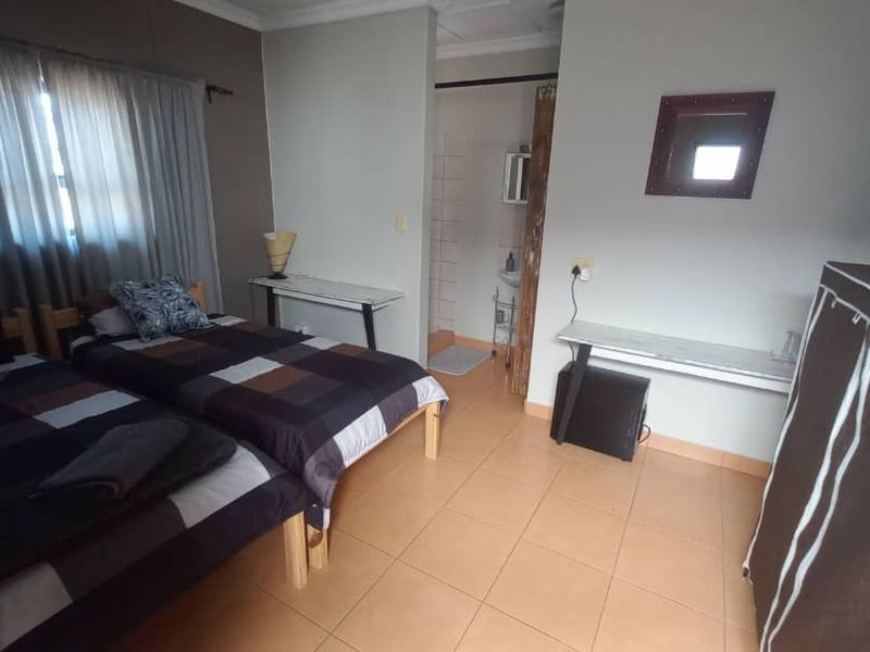 A functional bedroom featuring tiled flooring, neutral wall tones, and direct access to an en-suite bathroom area.