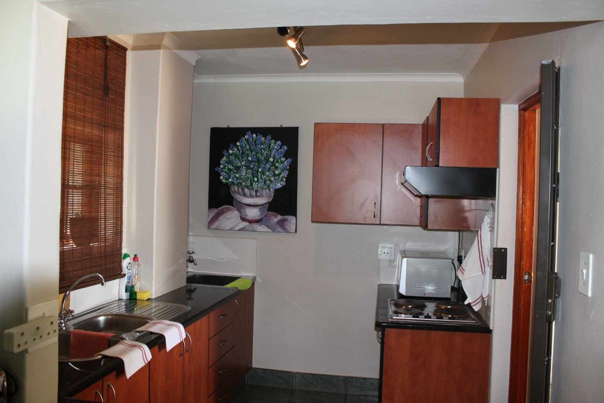 Compact kitchen featuring dark laminate cabinetry, granite countertops, a stainless steel sink, and a built-in electric hob with an extractor fan.