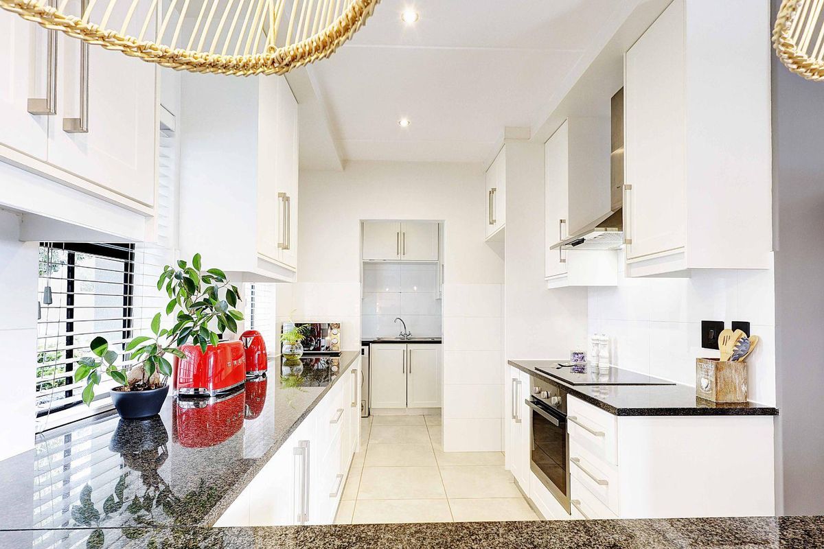 Modern kitchen featuring white cabinetry, dark granite countertops, built-in oven, electric hob, and a separate scullery area with additional sink and storage.