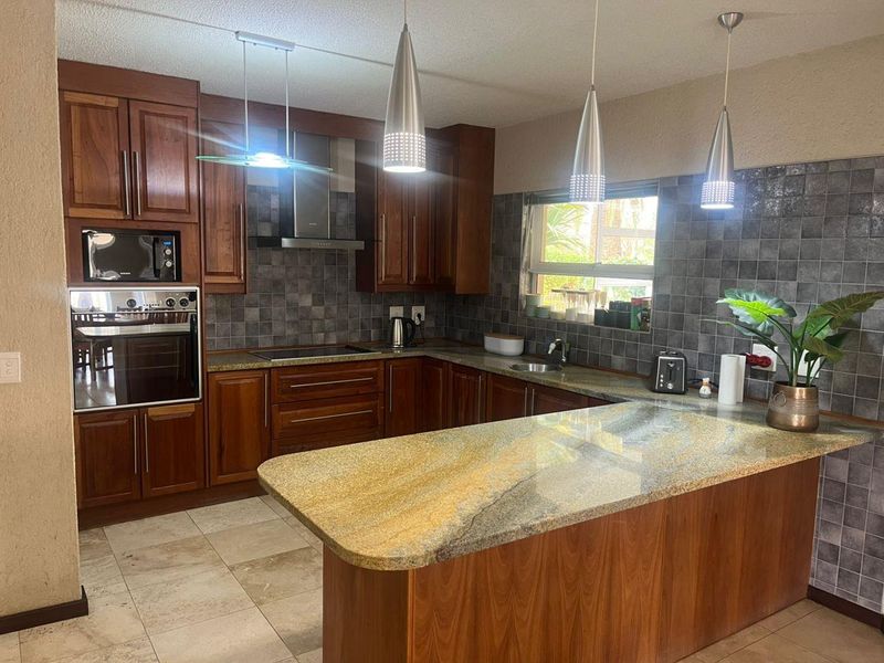 A well-maintained kitchen featuring rich wooden cabinetry, granite countertops, built-in appliances, and a functional breakfast bar layout with modern pendant lighting.