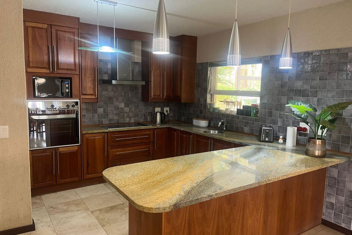A well-maintained kitchen featuring rich wooden cabinetry, granite countertops, built-in appliances, and a functional breakfast bar layout with modern pendant lighting.