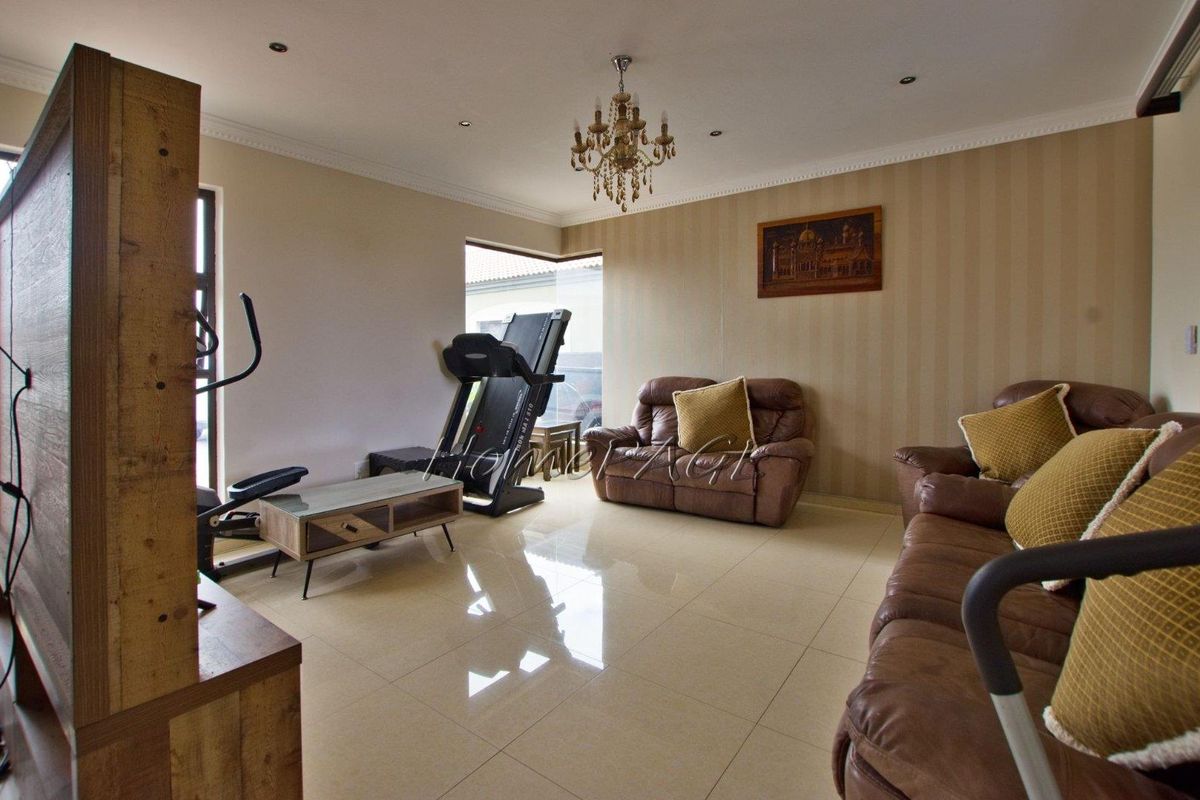 Spacious living area featuring polished floor tiles, recessed downlighting, and decorative crown molding, offering a versatile layout for relaxation and home fitness.