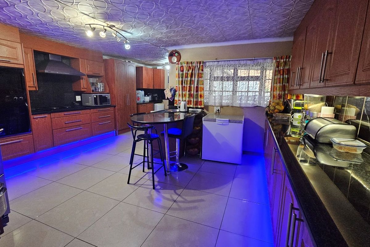 Spacious kitchen featuring extensive wooden cabinetry, granite countertops, tiled flooring, and a textured ceiling with integrated lighting.