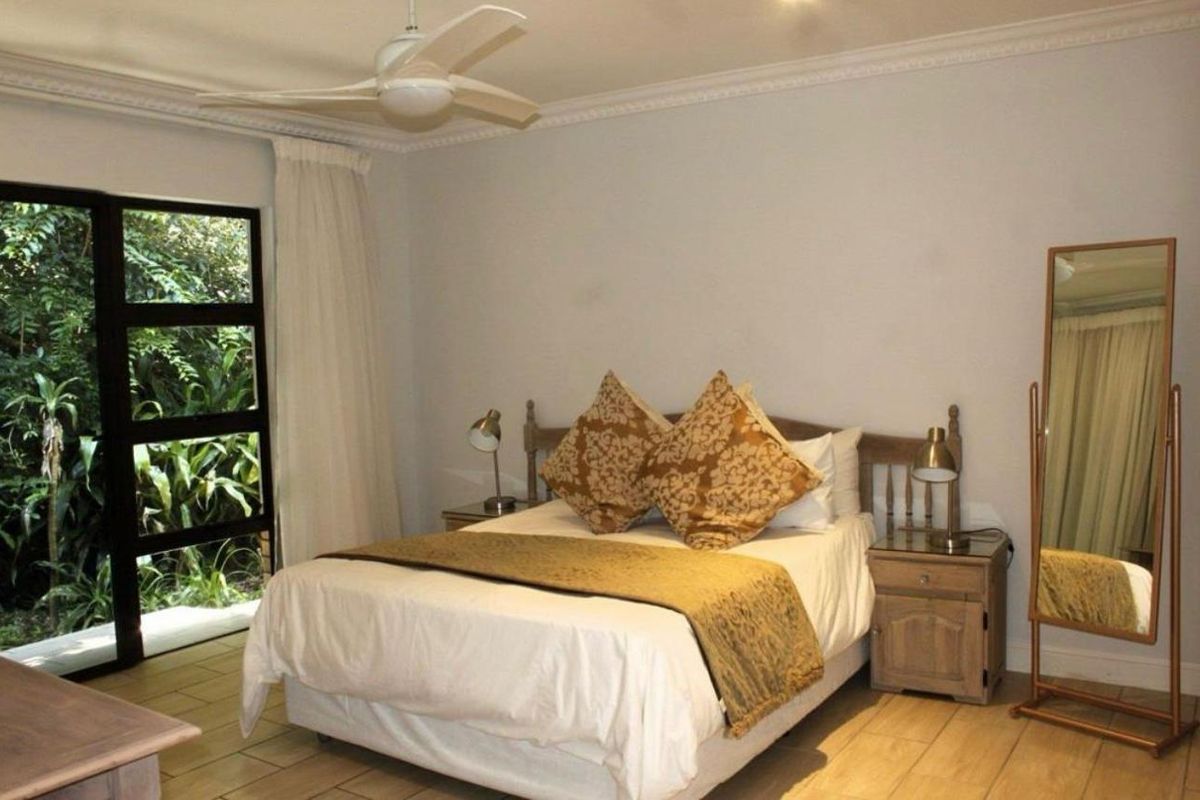 A well-lit bedroom featuring tiled flooring, a ceiling fan, and large glass sliding doors providing direct access to the garden area.