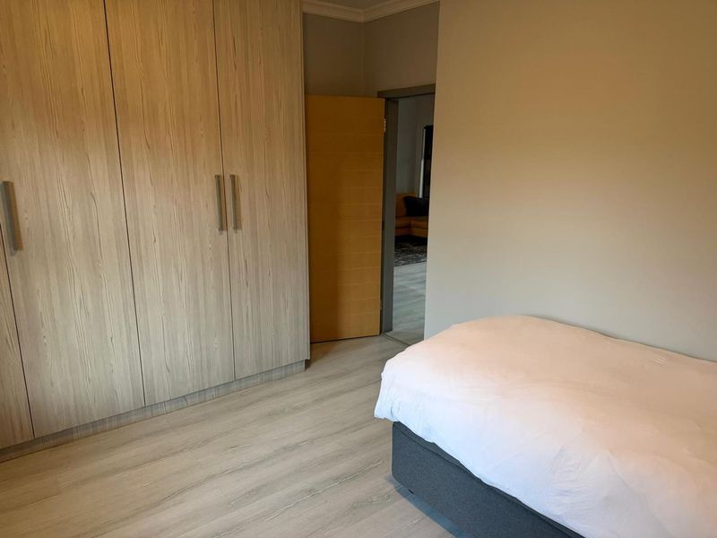 A well-maintained bedroom featuring light wood-grain built-in cupboards and modern laminate flooring, with a neutral color palette throughout.