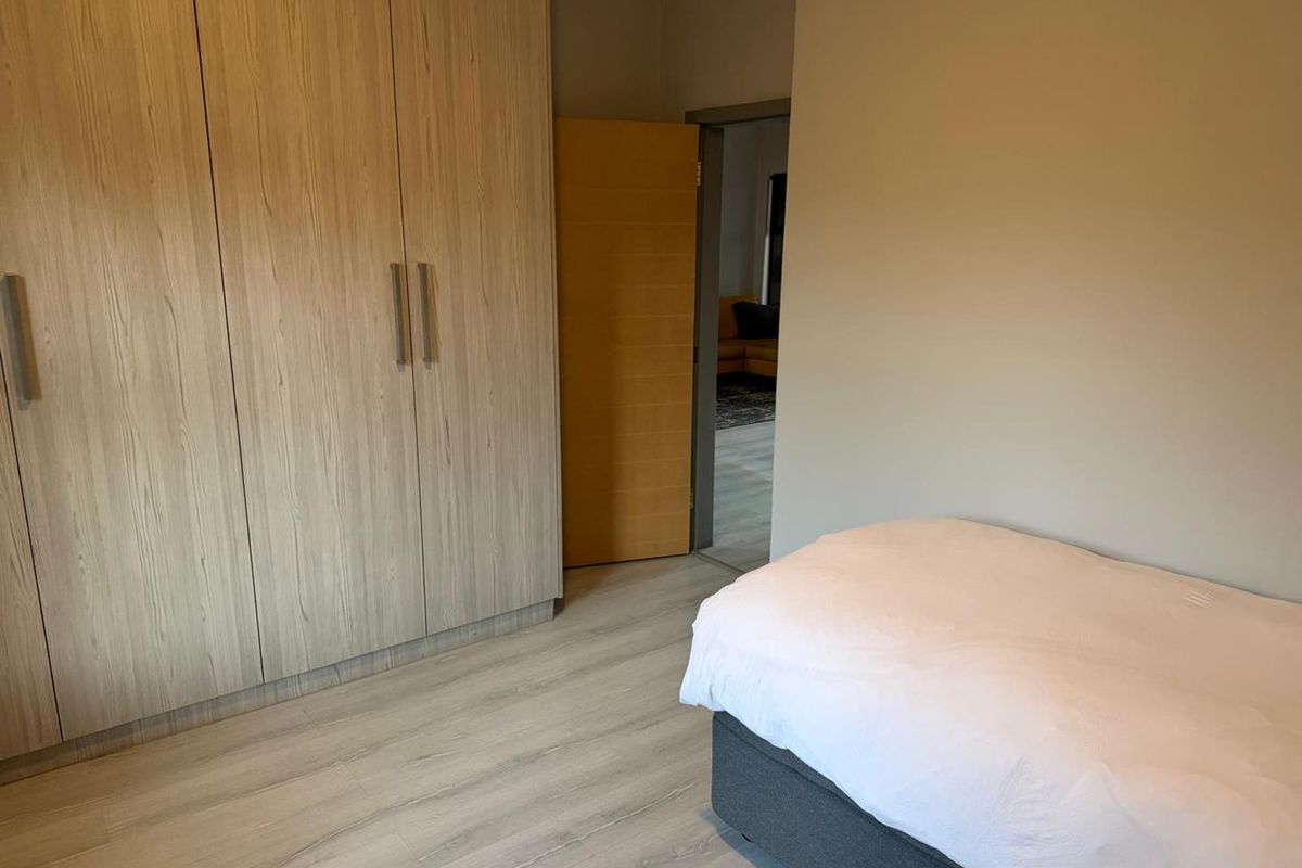 A well-maintained bedroom featuring light wood-grain built-in cupboards and modern laminate flooring, with a neutral color palette throughout.