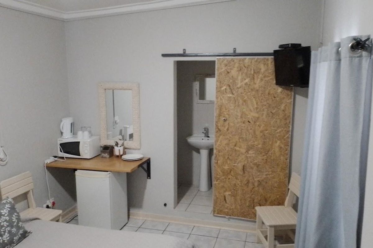 A compact guest bedroom featuring a small kitchenette area and an en-suite bathroom accessed via a sliding door.