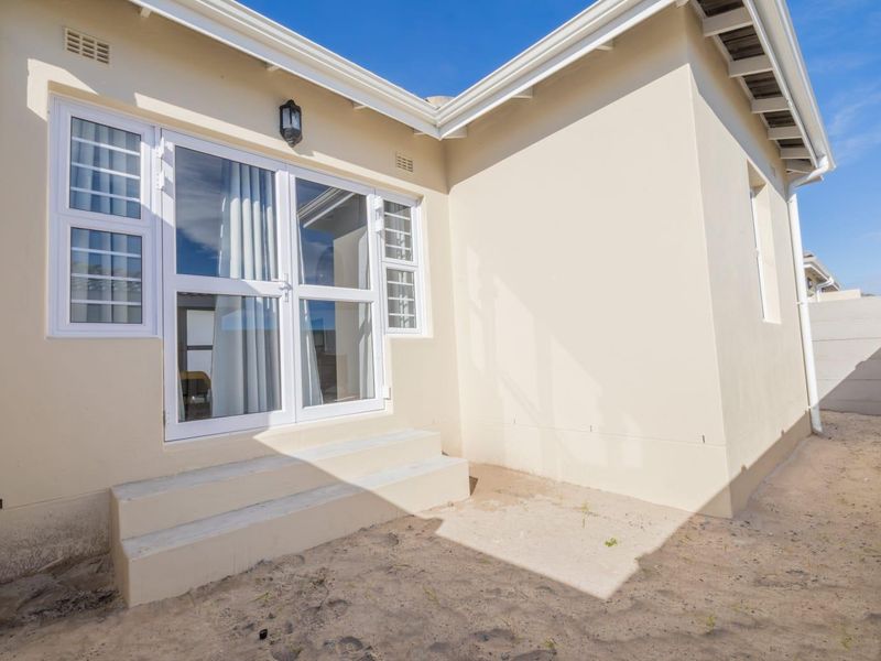 Rear exterior view of the property featuring white aluminium framed glass doors, concrete steps, and an unlandscaped sandy backyard area.