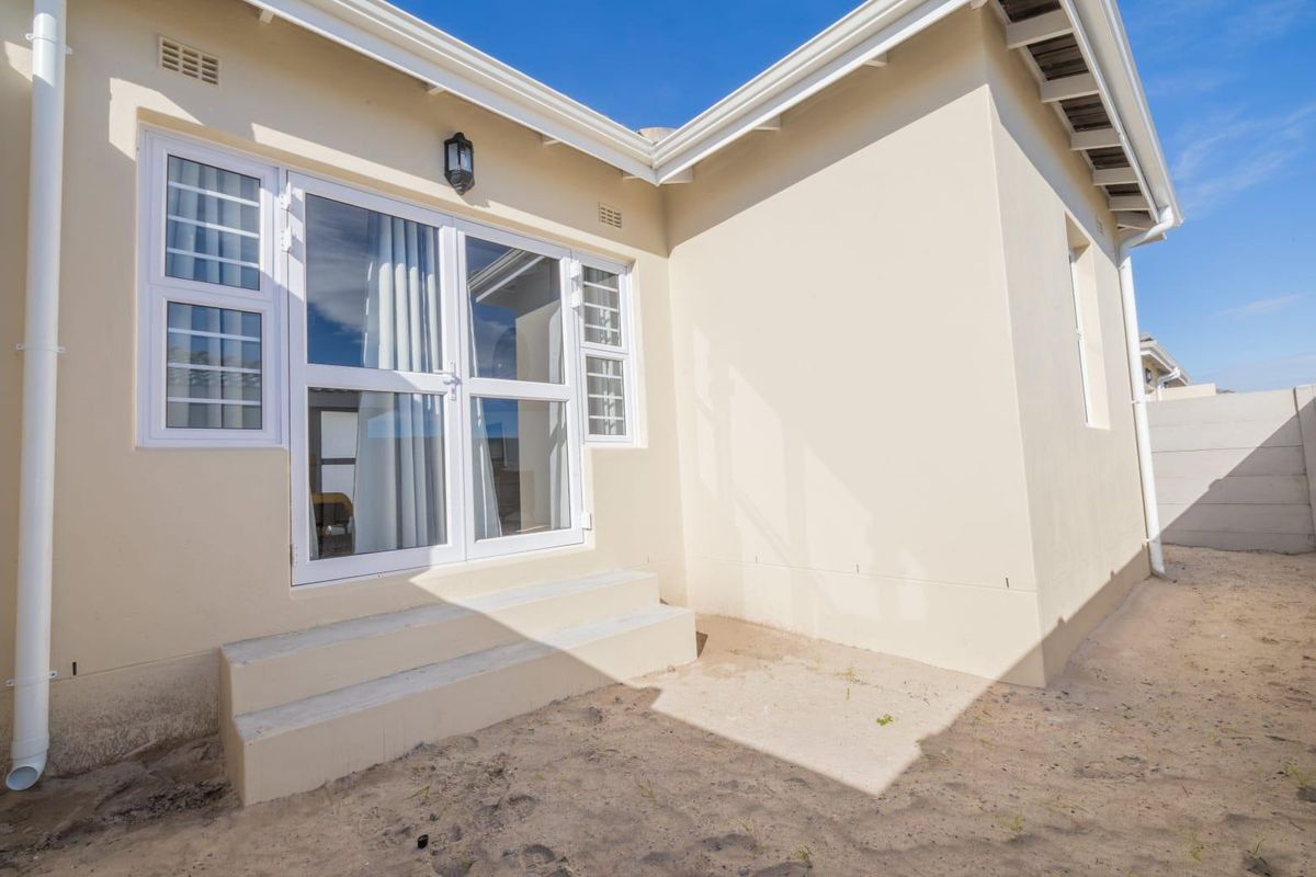 Rear exterior view of the property featuring white aluminium framed glass doors, concrete steps, and an unlandscaped sandy backyard area.