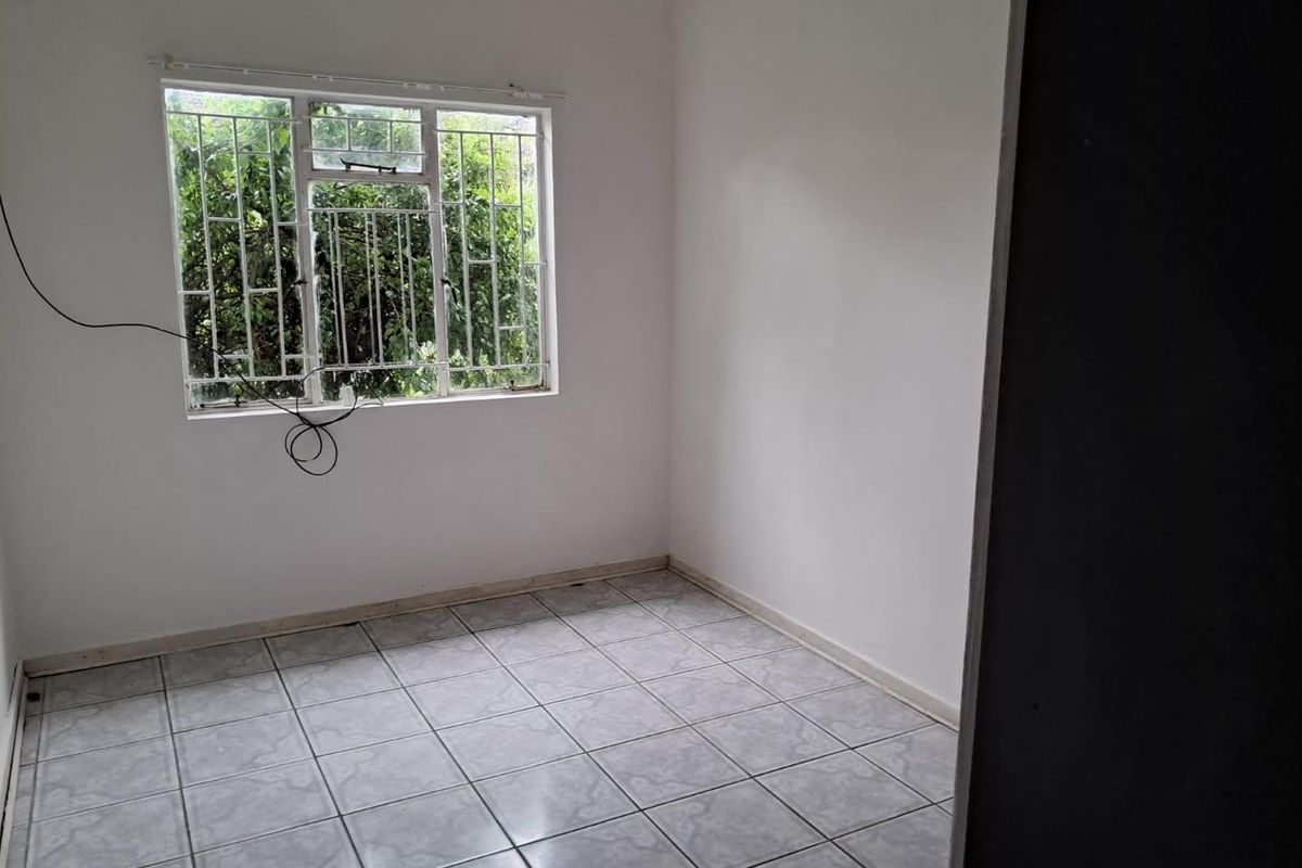 A vacant bedroom featuring tiled flooring and a window fitted with security bars.