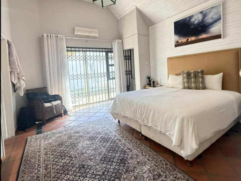 Spacious bedroom featuring vaulted ceilings, terracotta flooring, and a security gate leading to an outdoor area, equipped with a wall-mounted air conditioning unit.