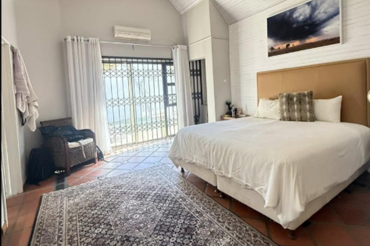 Spacious bedroom featuring vaulted ceilings, terracotta flooring, and a security gate leading to an outdoor area, equipped with a wall-mounted air conditioning unit.