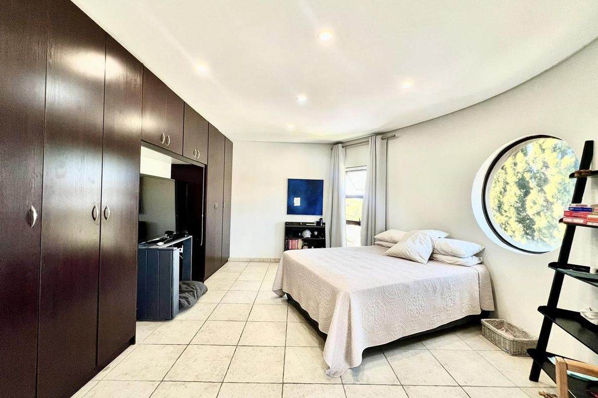 Spacious bedroom featuring large built-in dark wood cabinetry, tiled flooring, recessed ceiling lighting, and a distinctive circular window.