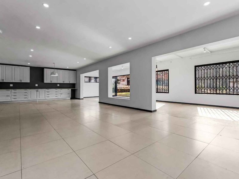 Spacious open-plan living area featuring neutral tiled flooring, recessed lighting, and a modern kitchen with ample built-in cabinetry.