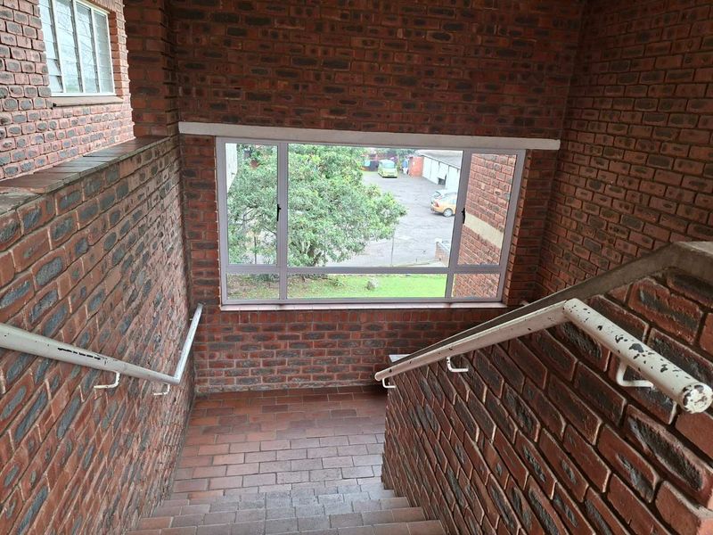 A functional apartment stairwell featuring exposed brick walls, tiled steps, and metal handrails with a view overlooking the exterior grounds.