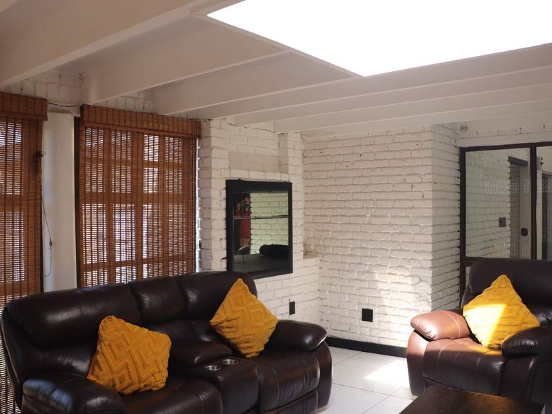 A living room featuring white painted exposed brick walls, a large skylight providing natural light, and tiled flooring.
