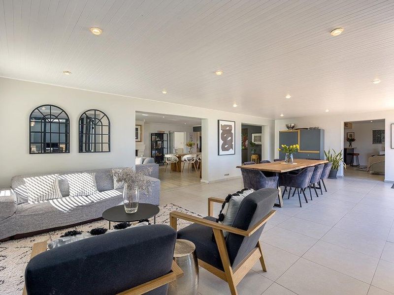 Spacious open-plan living and dining area featuring neutral tiled flooring, recessed downlighting, and a clean, modern aesthetic throughout the connected living spaces.