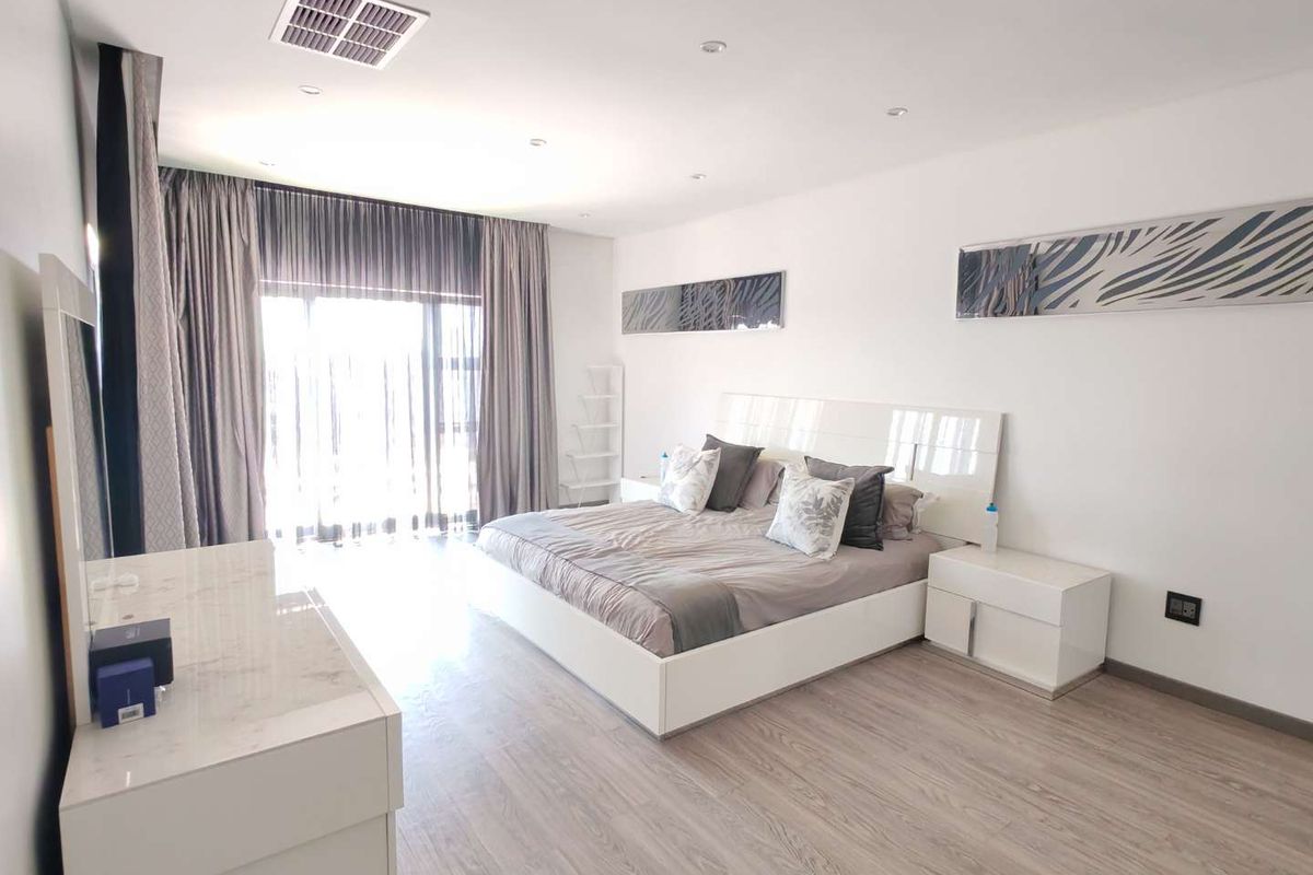 A spacious, well-lit bedroom featuring modern laminate flooring, recessed ceiling lighting, and large sliding glass doors leading to an outdoor area.