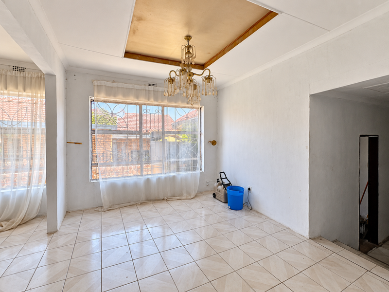 Spacious living area featuring ceramic floor tiles, a decorative recessed ceiling, and large windows with security bars, offering a bright and open layout.