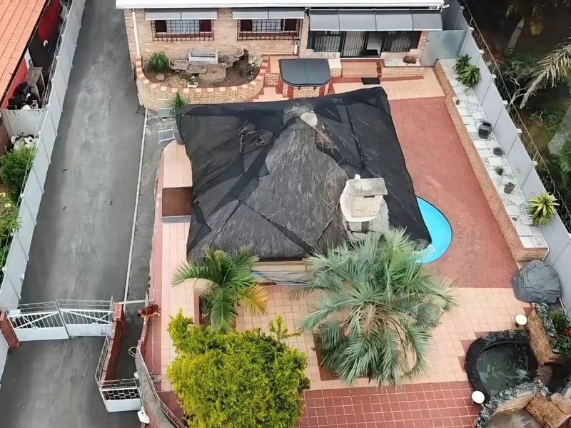 Aerial view of the property featuring a swimming pool, a paved patio area, and a thatched lapa with an integrated outdoor fireplace.