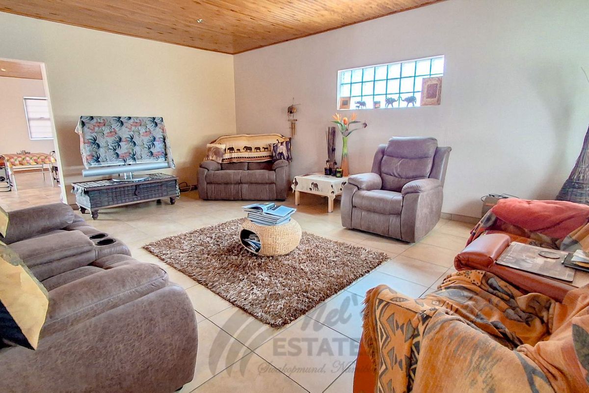 Spacious living room featuring tiled flooring and a timber-paneled ceiling, with a glass block window providing natural light.