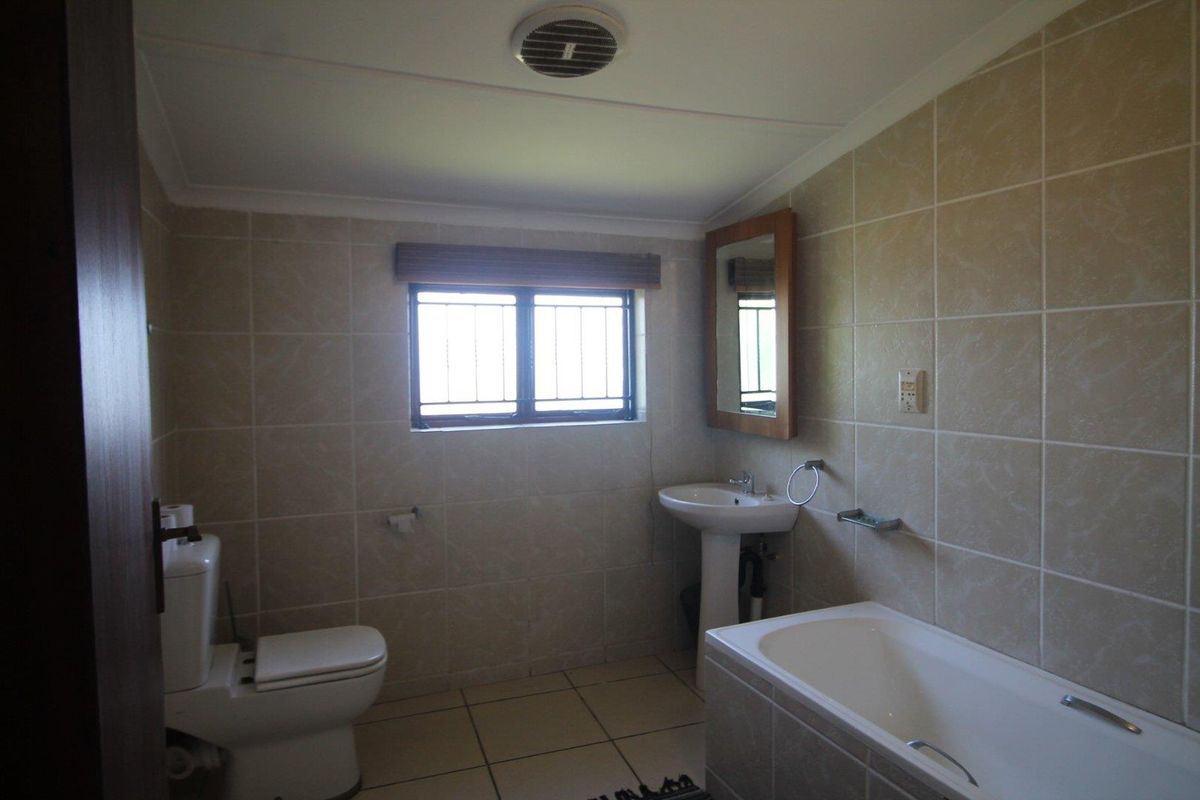 A functional bathroom featuring a pedestal sink, a bathtub, a toilet, and neutral wall tiling with a window for natural light.