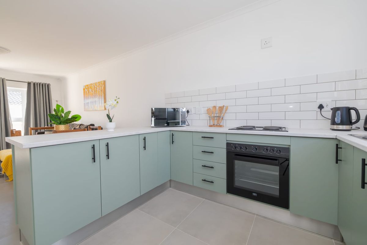 Modern kitchen featuring sage green cabinetry, white subway tile backsplash, built-in oven, gas hob, and light-toned floor tiles in an open-plan layout.