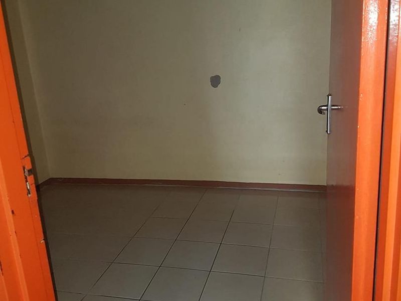 An empty bedroom featuring tiled flooring and neutral walls, requiring minor cosmetic repairs to the wall surface and door frame.