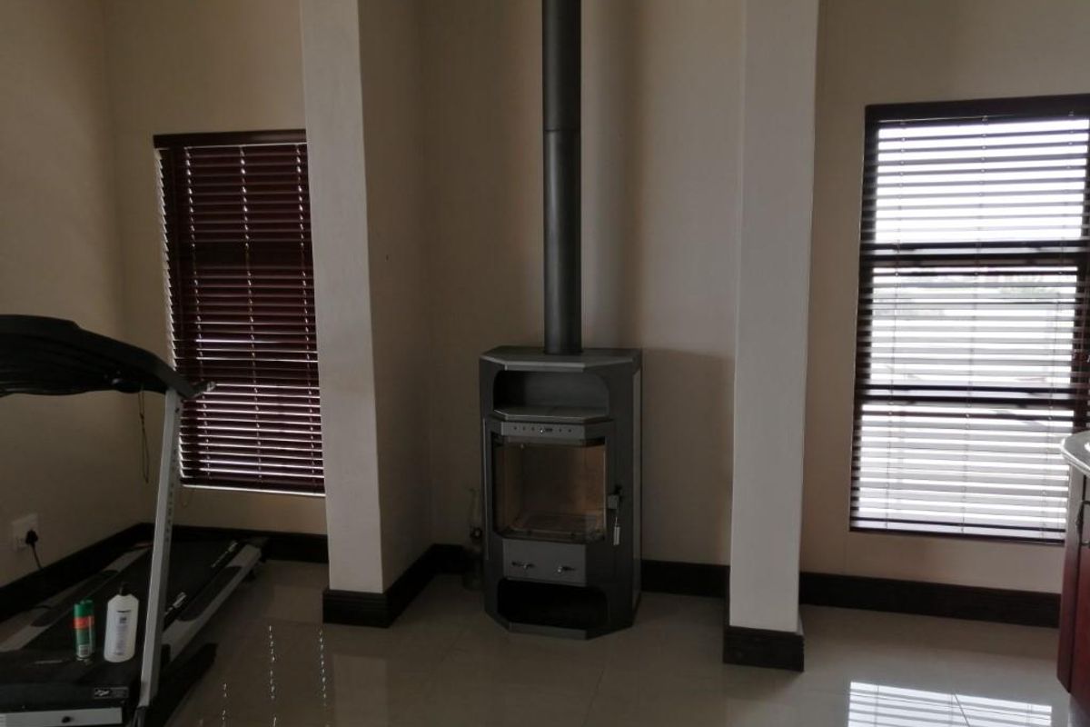 A living area featuring a built-in fireplace with a flue, tiled flooring, and large windows fitted with horizontal blinds.