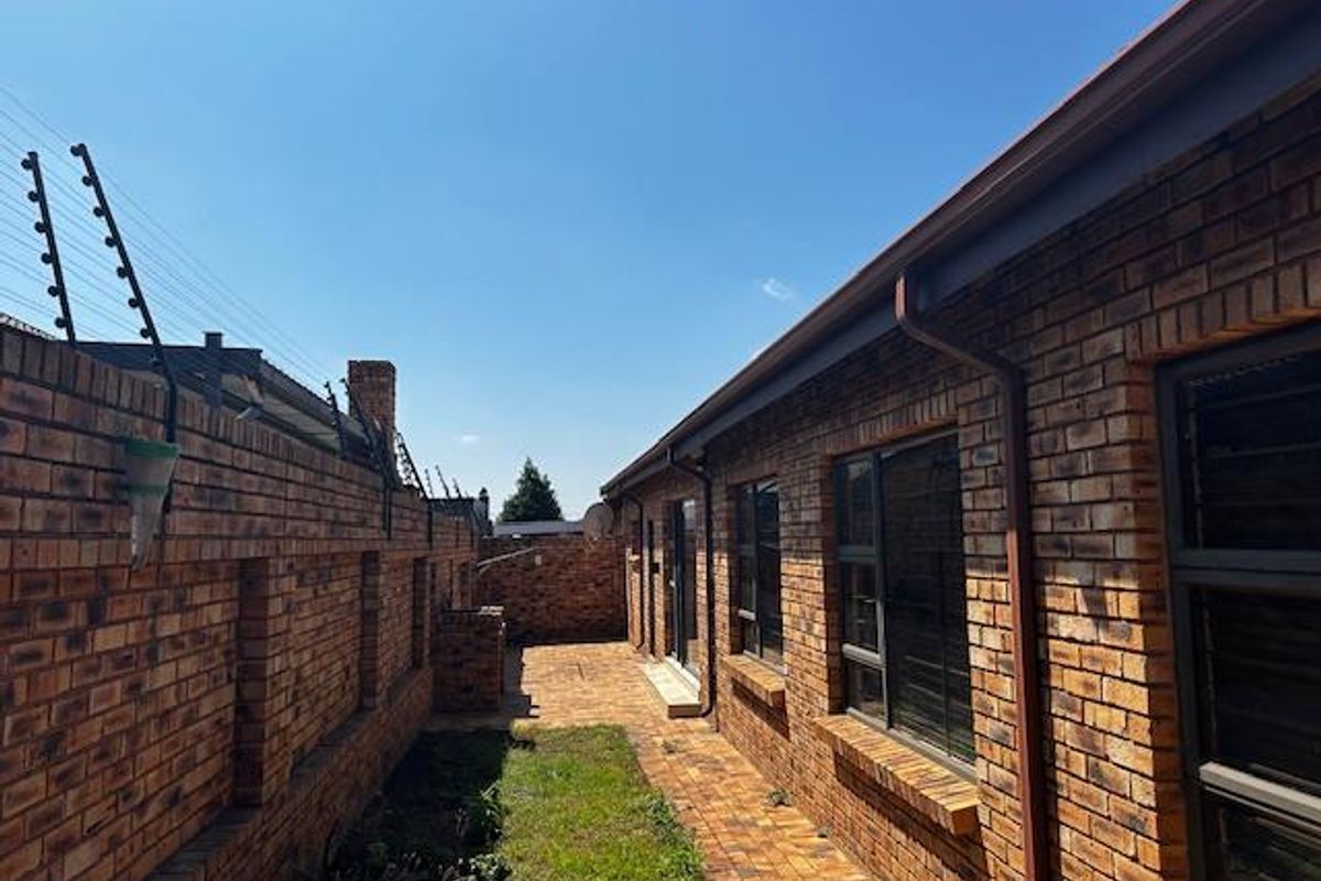 A side exterior view of the cluster property featuring face-brick walls, paved pathways, and perimeter security fencing.